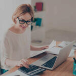 Small business owner outsourcing a bookkeeper working on laptop with financial reports and calculator on desk