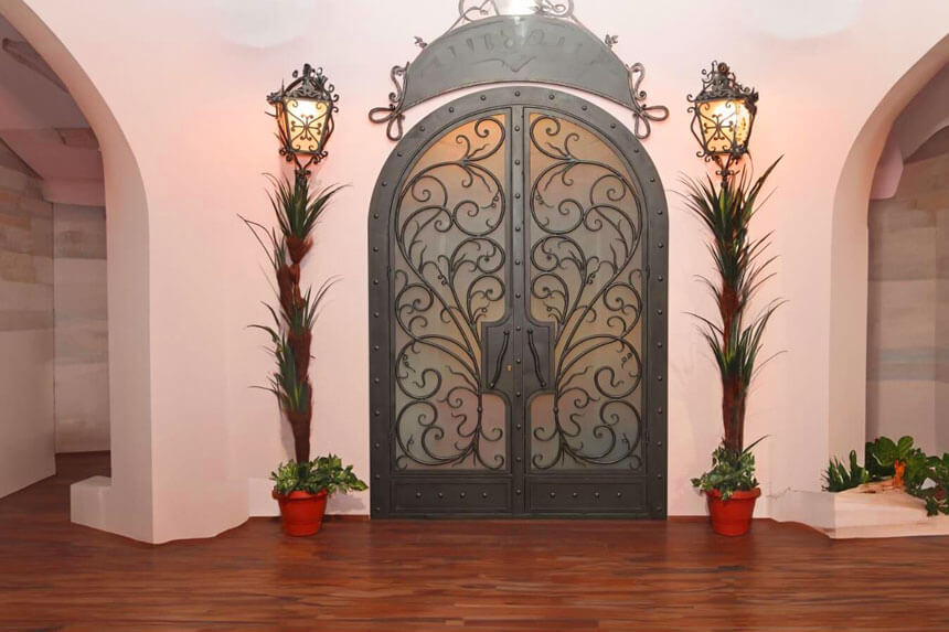 Front wrought iron doors with decorative scrollwork and glass panels installed on luxury home entrance
